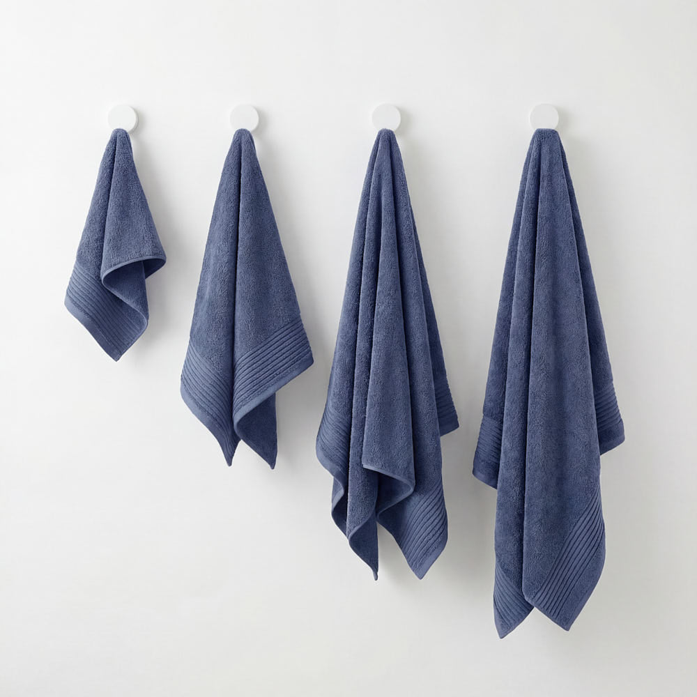 Four navy blue plush towels set with ribbed edges hanging neatly on white hooks for a stylish bathroom look