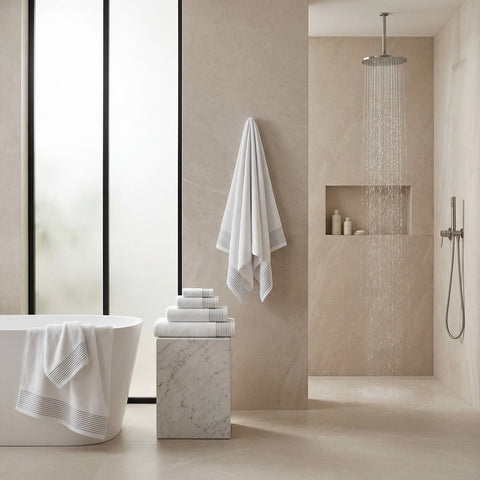 White plush towels set with subtle gray striped border hanging neatly on wall for bathroom use