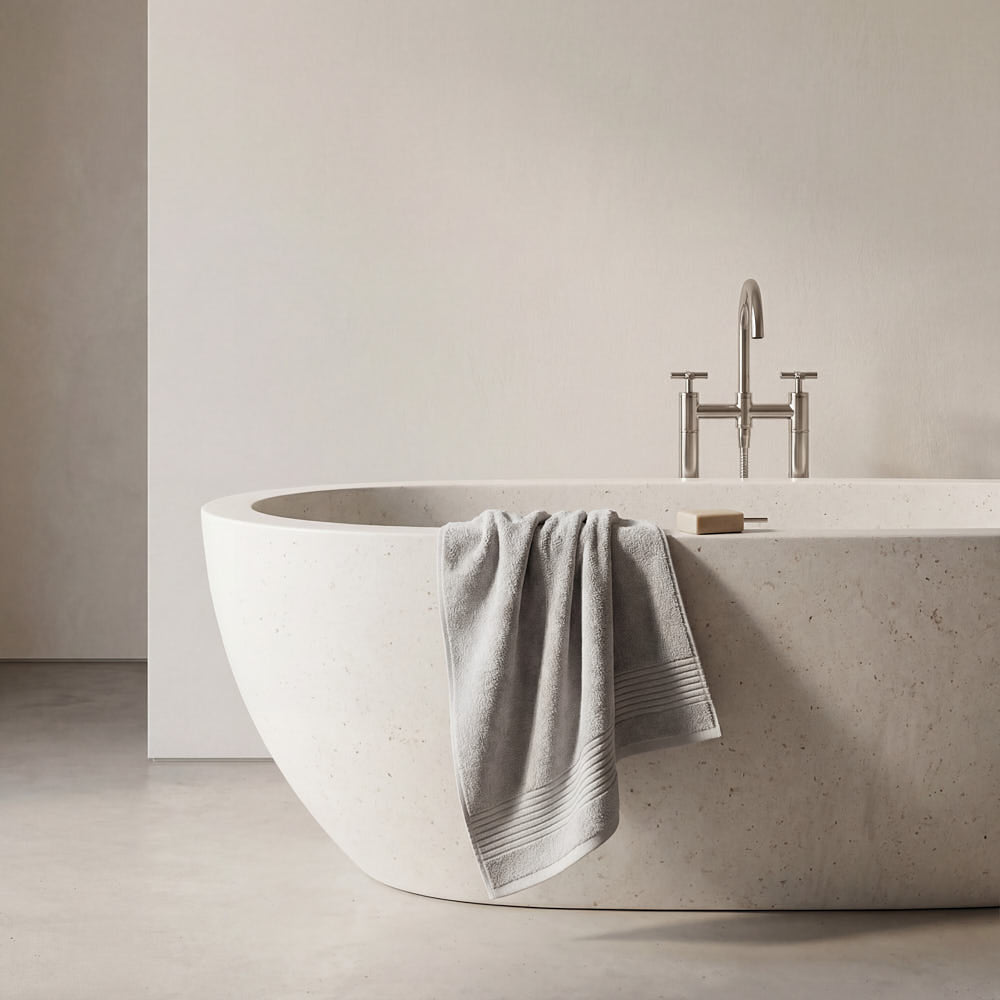 A soft gray plush towel with ribbed texture draped over the edge of a modern white stone bathtub