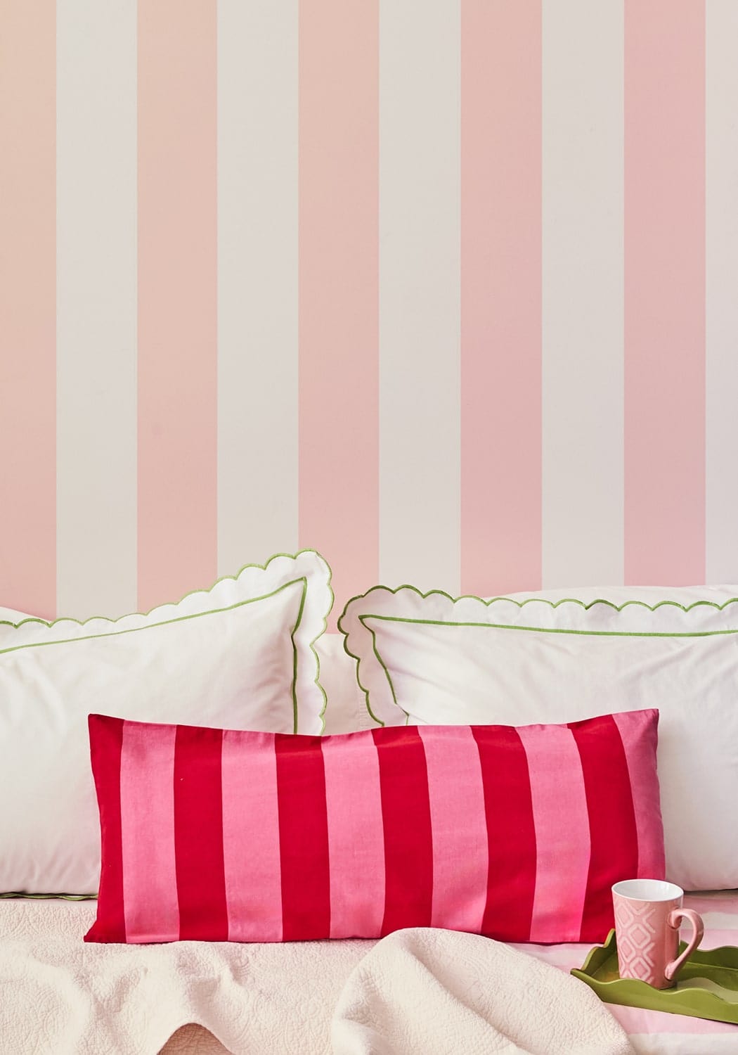 A vibrant pink and red striped satin lumbar cushion cover with scalloped edges resting on white pillows