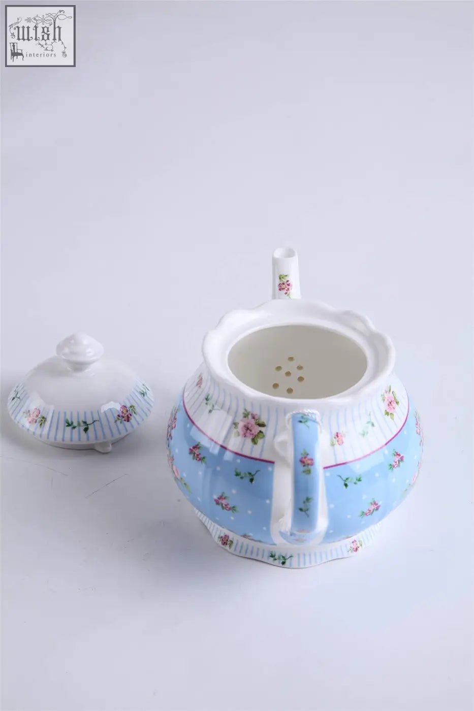 A delicate porcelain teapot with pink floral patterns and white scalloped edges in a blue teapot sugar bowl set