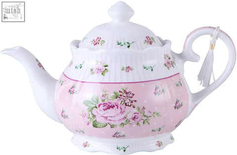 A delicate porcelain teapot in soft pink with rose patterns, part of a shabby chic set including sugar bowl and cream milk jug