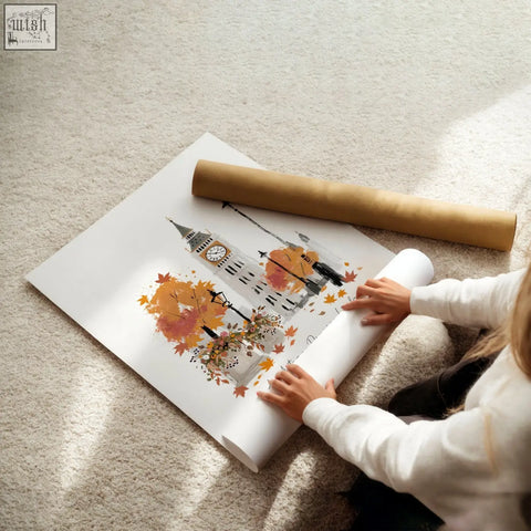 A white poster art print featuring big ben surrounded by orange autumn leaves rolled out on a carpeted floor