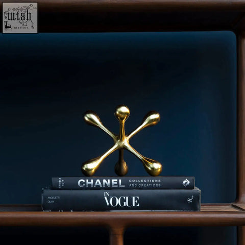 Gold finish prato jack sculpture with four teardrop arms on a sphere resting on stacked black books