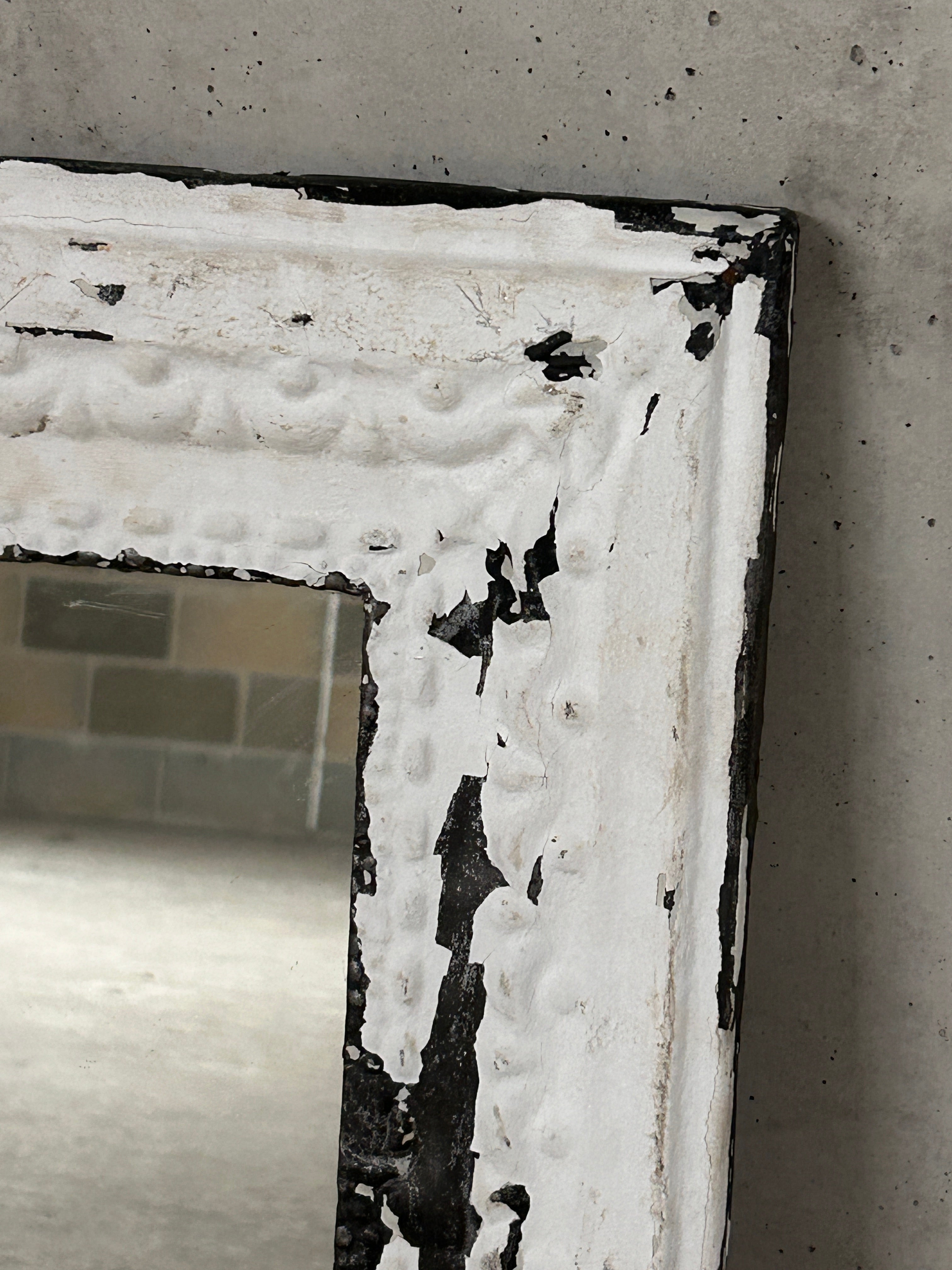 A distressed white-framed pressed tin ceiling tile mirror with chipped paint revealing black metal underneath