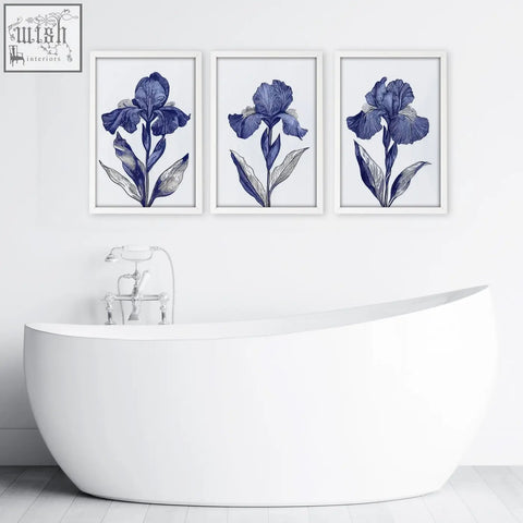 Three framed blue iris botanical wall art prints hang above a white freestanding bathtub in bathroom decor