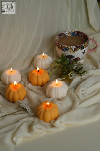Six pumpkin shaped candles in white and orange with lit wicks glowing warm perfect for pumpkin spice vibes