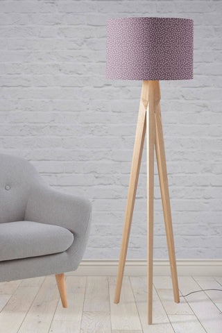 A modern line tripod table lamp with a purple lampshade in mauve fabric and light wood legs