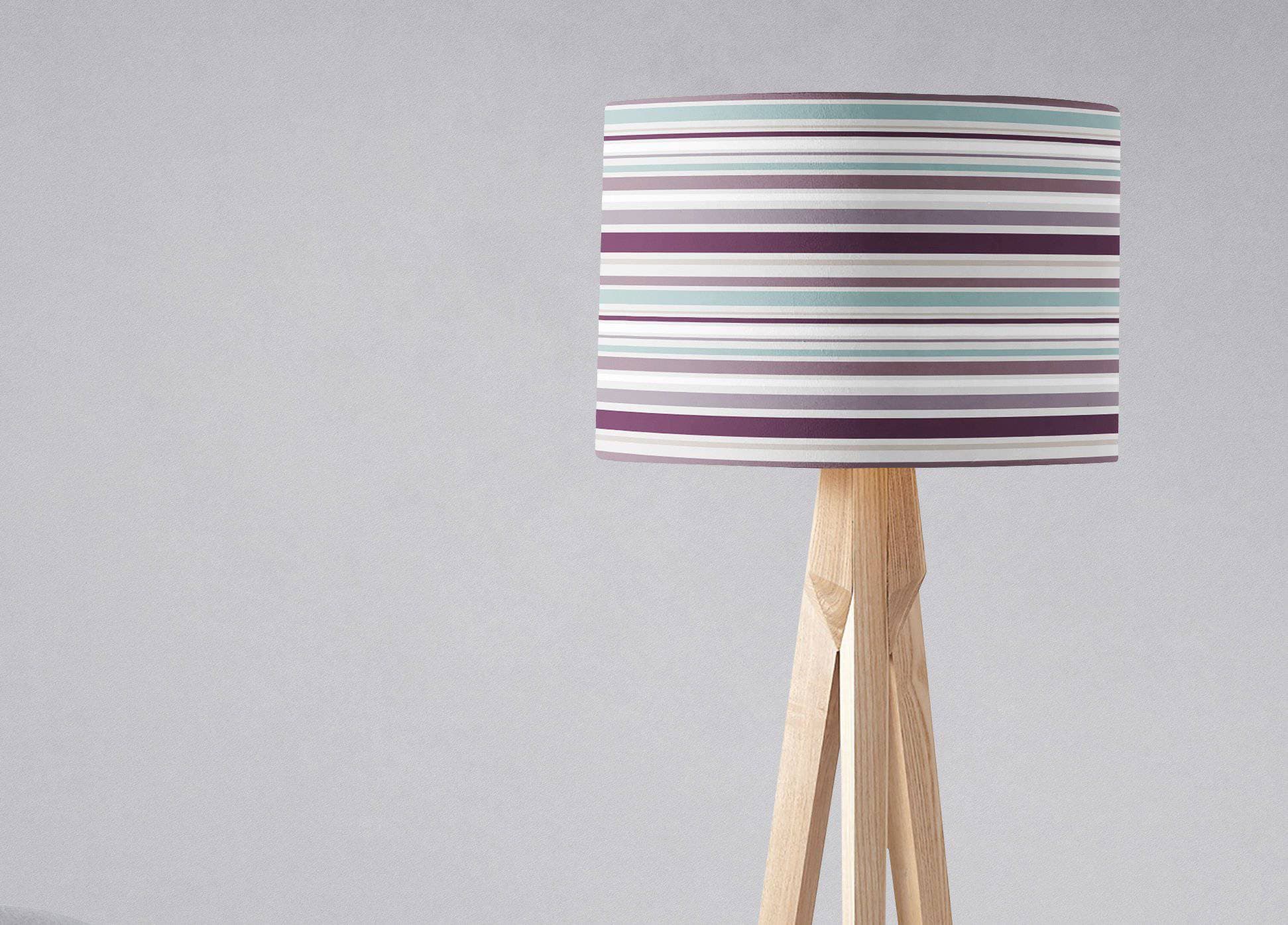 Purple striped lampshade with horizontal purple teal and white stripes on a light wood tripod table lamp base