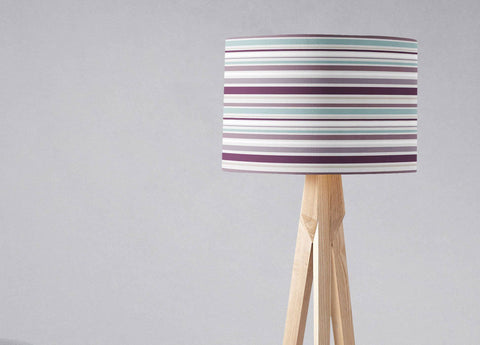 Purple striped lampshade with horizontal purple teal and white stripes on a light wood tripod table lamp base