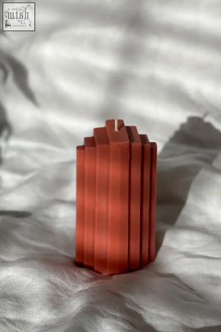 A terracotta pyramid sculpted candle with geometric segments and a central wick for home decor