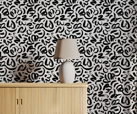 A sleek white ceramic quake table lamp with beige fabric shade on light wood cabinet with brushstroke wallpaper background