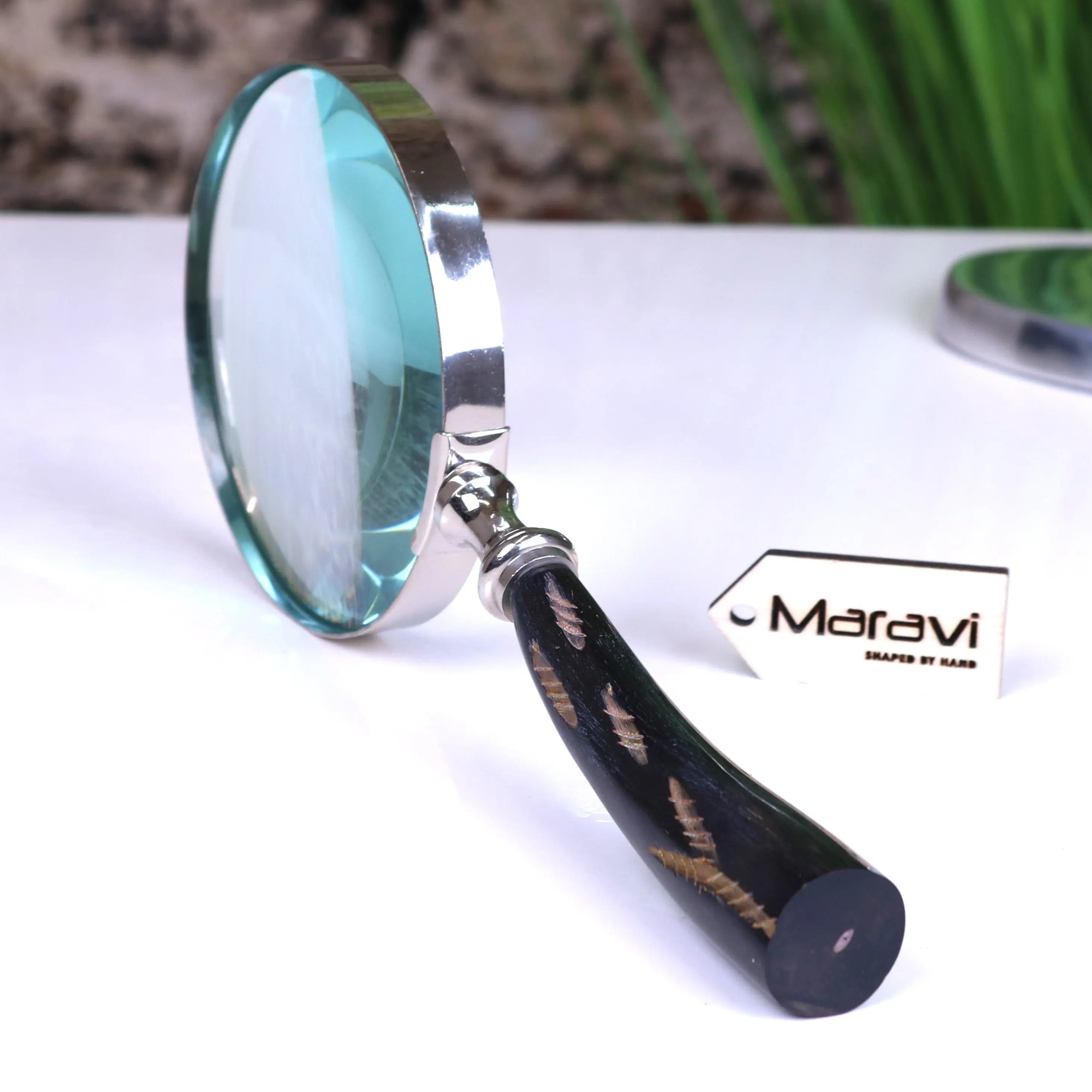 A sleek rada magnifying glass with a polished silver frame black handle and golden leaf inlays by maravi