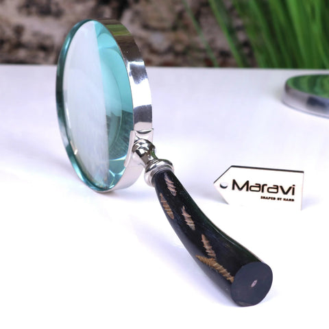 A sleek rada magnifying glass with a polished silver frame black handle and golden leaf inlays by maravi