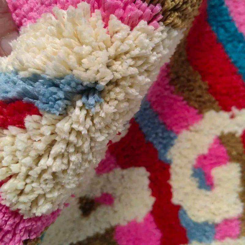A plush multicolored naked bathmat with fluffy pink red blue and cream pom-poms perfect for bathroom floors