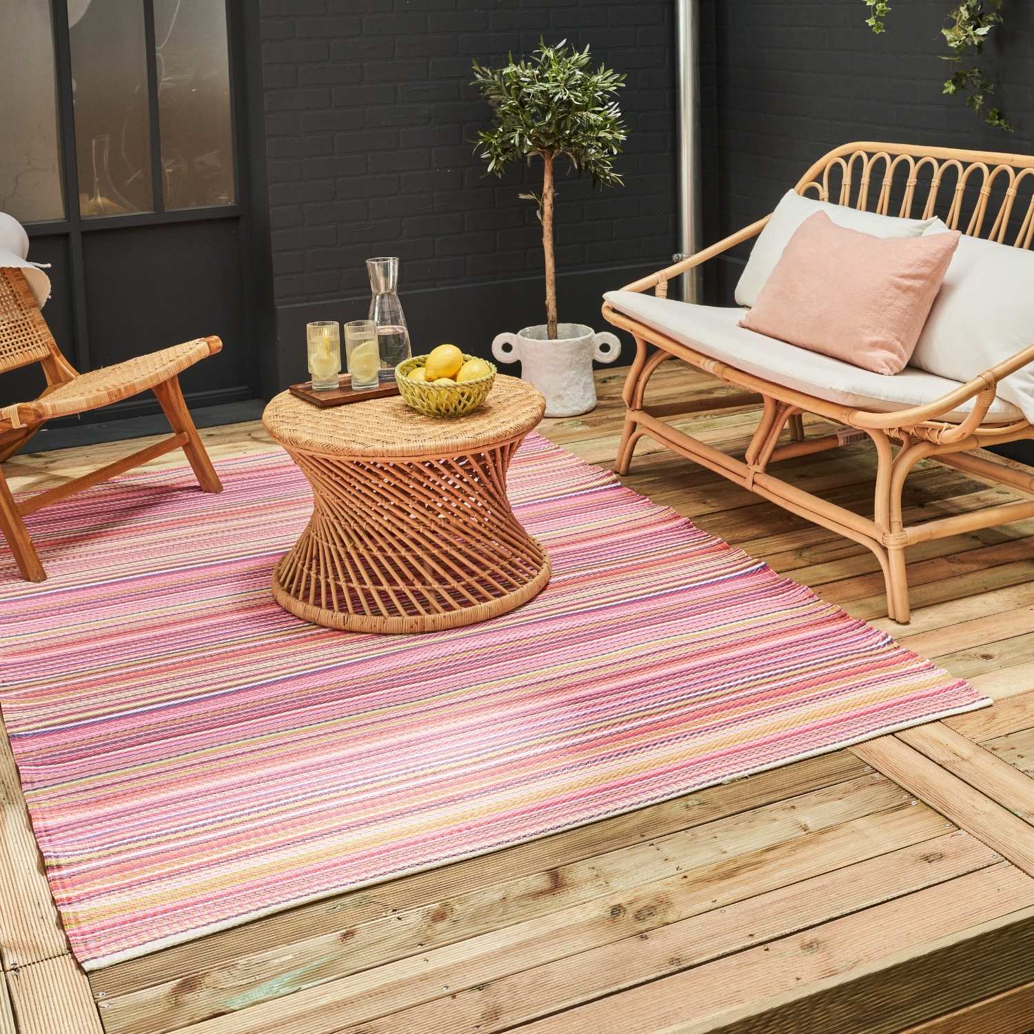 A vibrant rainbow outdoor rug pink with woven texture and horizontal stripes in pink purple and beige