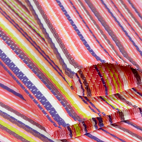 A vibrant rainbow outdoor rug pink with bold diagonal stripes in pink purple white and lime green woven design