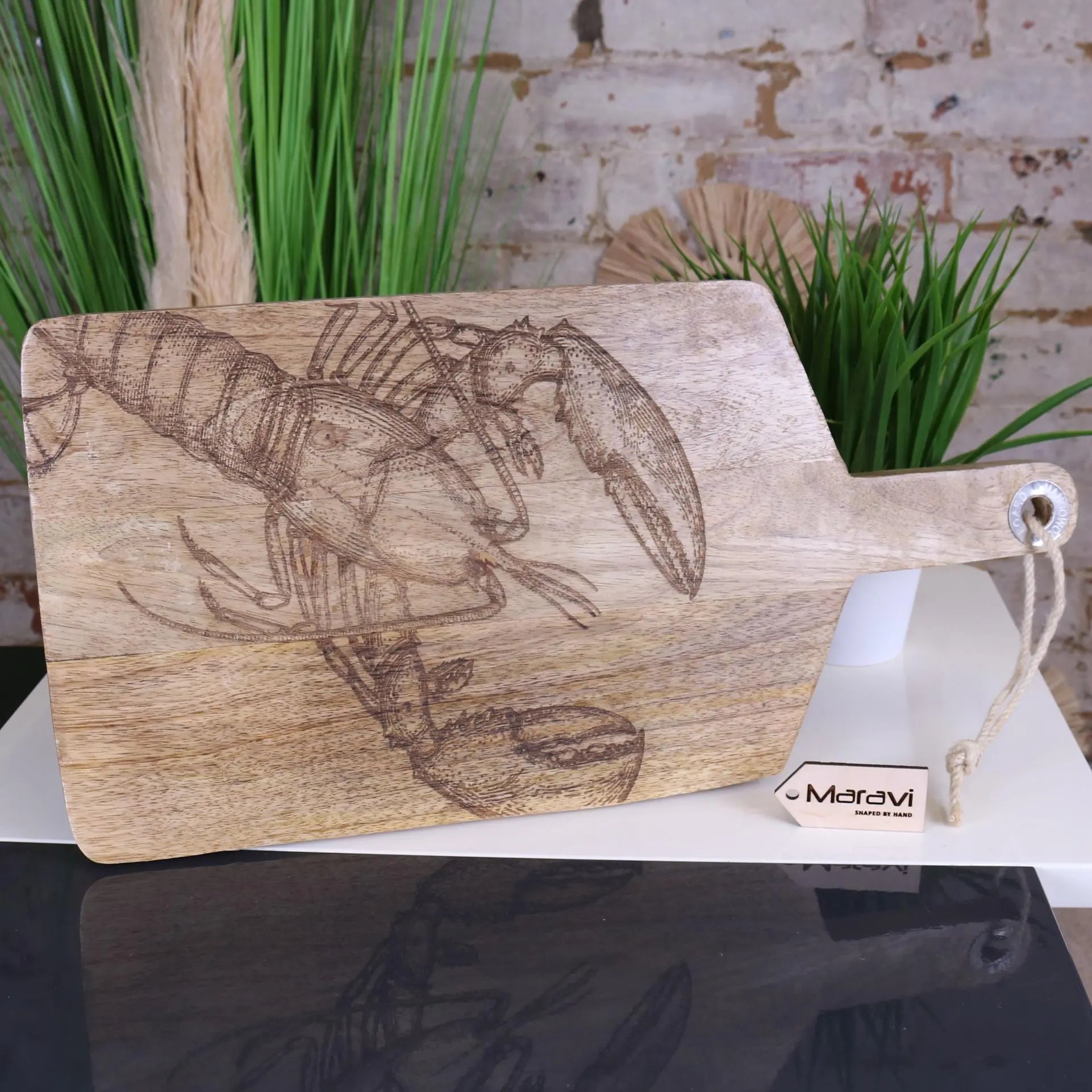 A light wooden serving platter board with a detailed engraved lobster design and metal ring handle by rateka