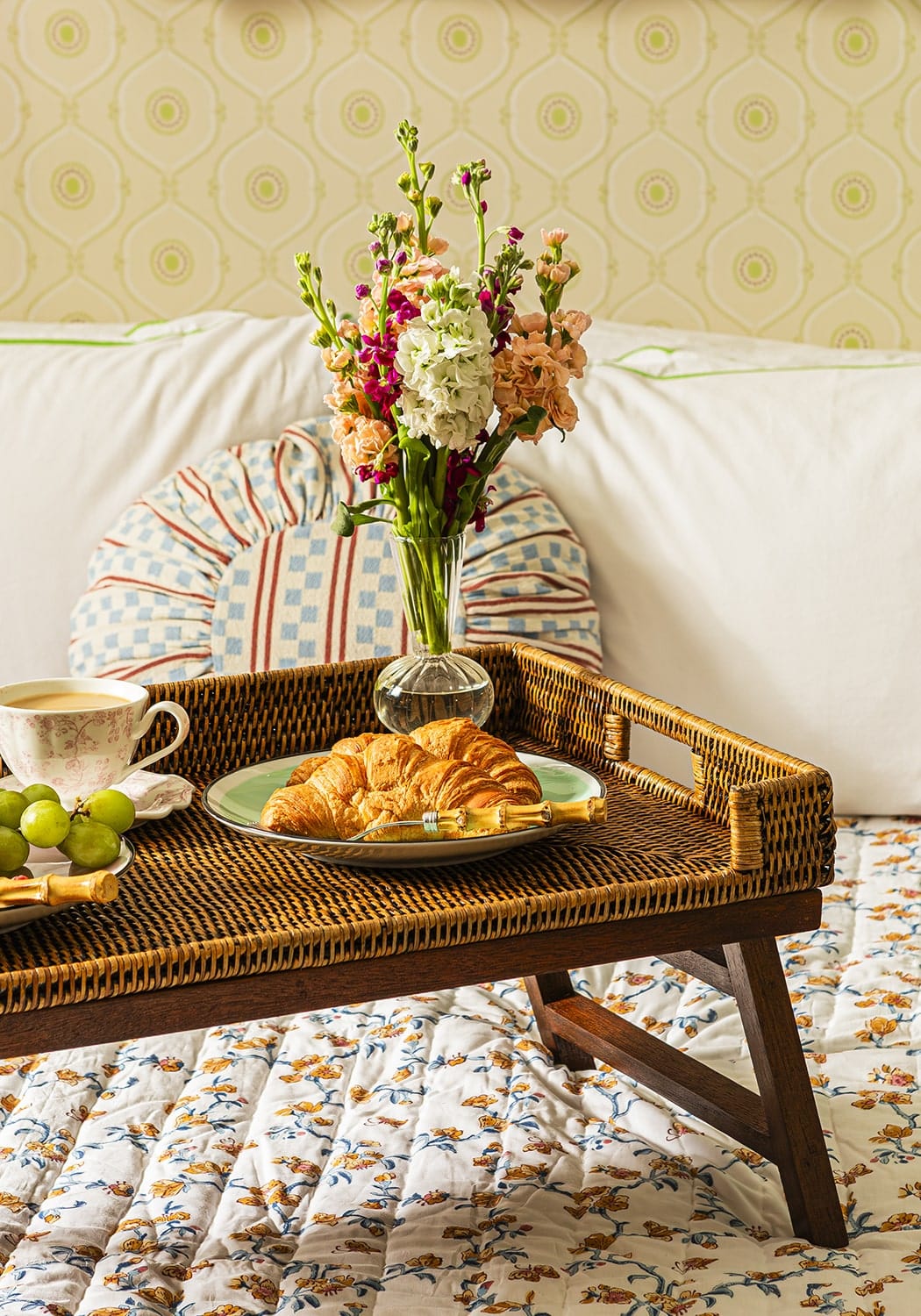 Brown woven rattan breakfast tray with wooden legs and a green plate holding croissants for rattan breakfast use