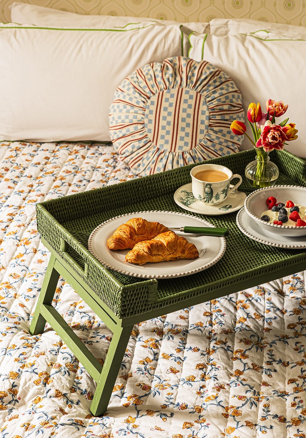 Green rattan breakfast tray with textured surface and foldable legs holding breakfast on a bed