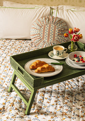 Green rattan breakfast tray with textured surface and foldable legs holding breakfast on a bed