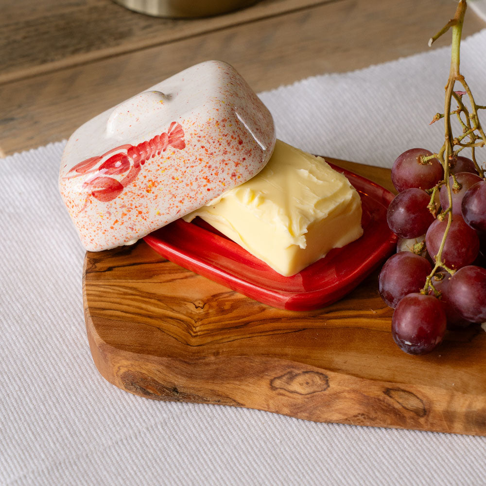 Cream-colored mini ceramic butter dish with red speckles and lobster design on matching red base holding butter