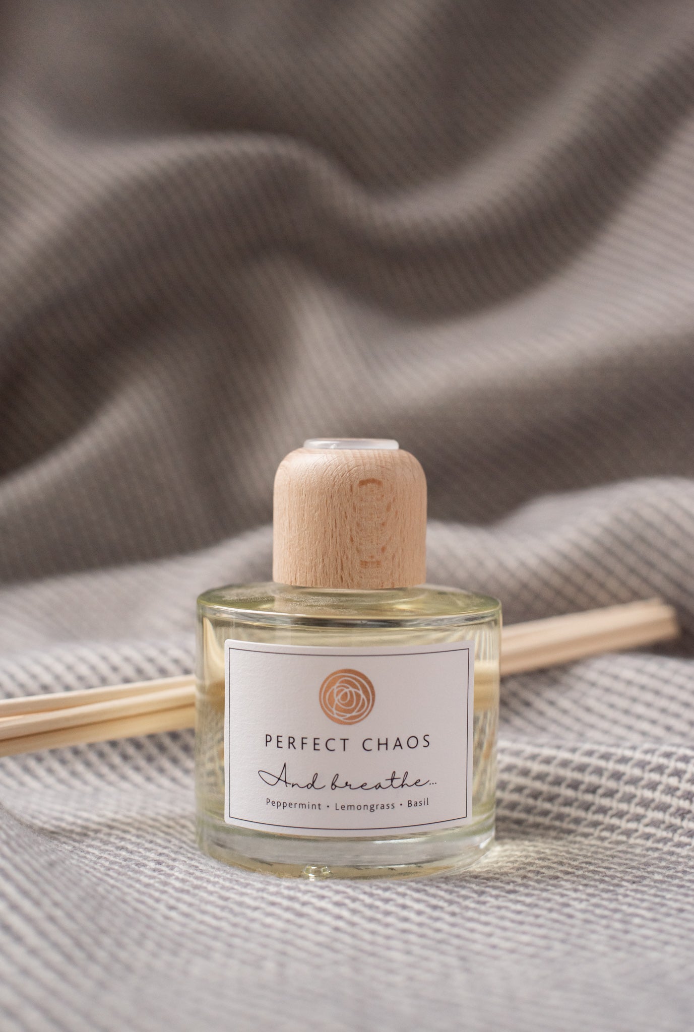 A clear glass reed diffuser bottle with light wood cap and pale yellow essential oils labeled and breathe