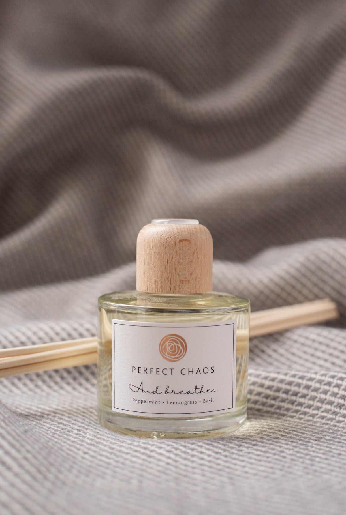 A clear glass reed diffuser bottle with light wood cap and pale yellow essential oils labeled and breathe