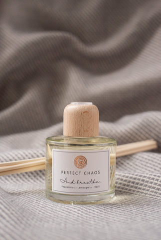 A clear glass reed diffuser bottle with light wood cap and pale yellow essential oils labeled and breathe