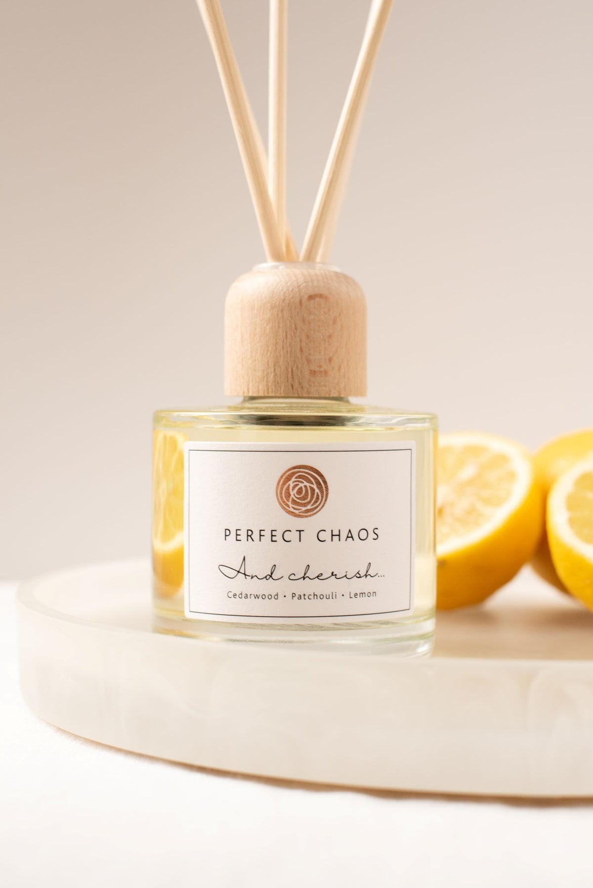 A clear glass reed diffuser with light wood cap and essential oils labeled perfect chaos and cherish with citrus scents
