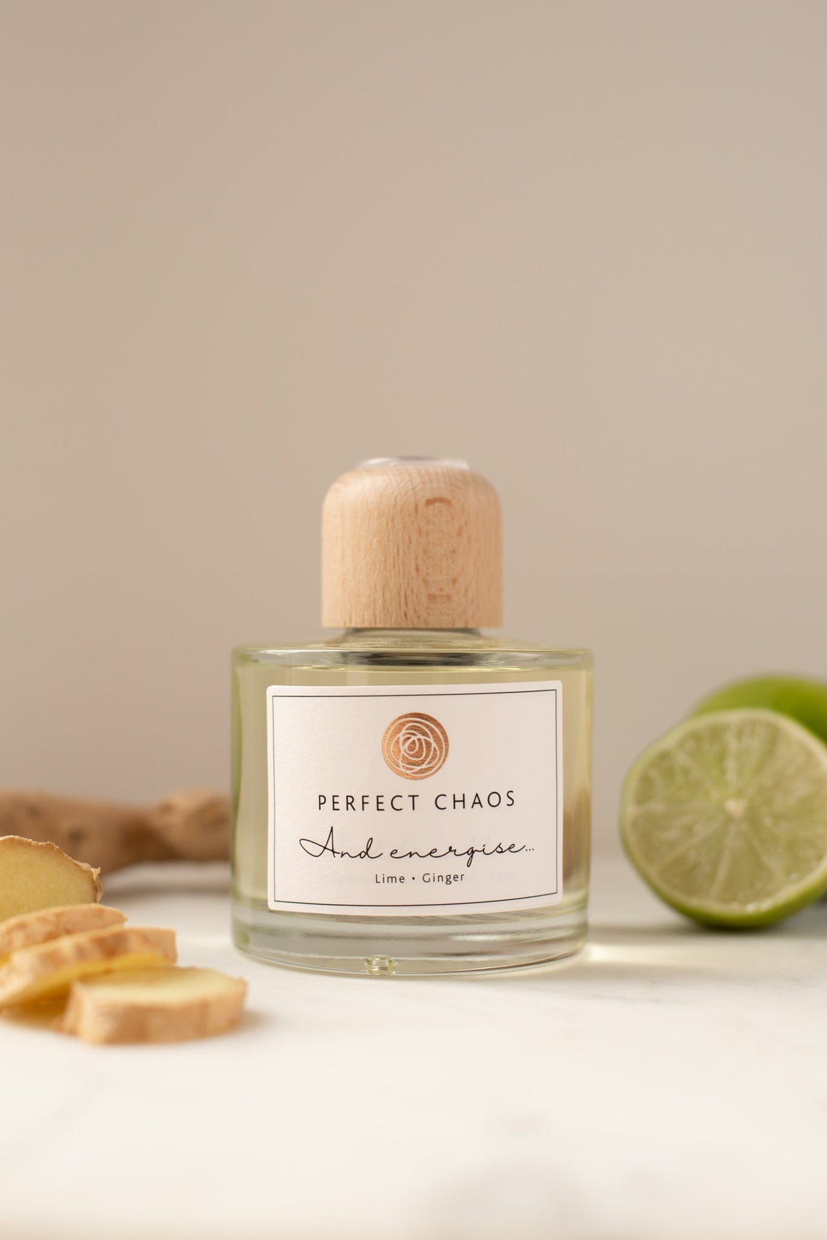 A clear glass reed diffuser with a light wood cap and energise lime and ginger scent sits beside sliced lime and ginger