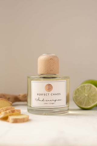 A clear glass reed diffuser with a light wood cap and energise lime and ginger scent sits beside sliced lime and ginger