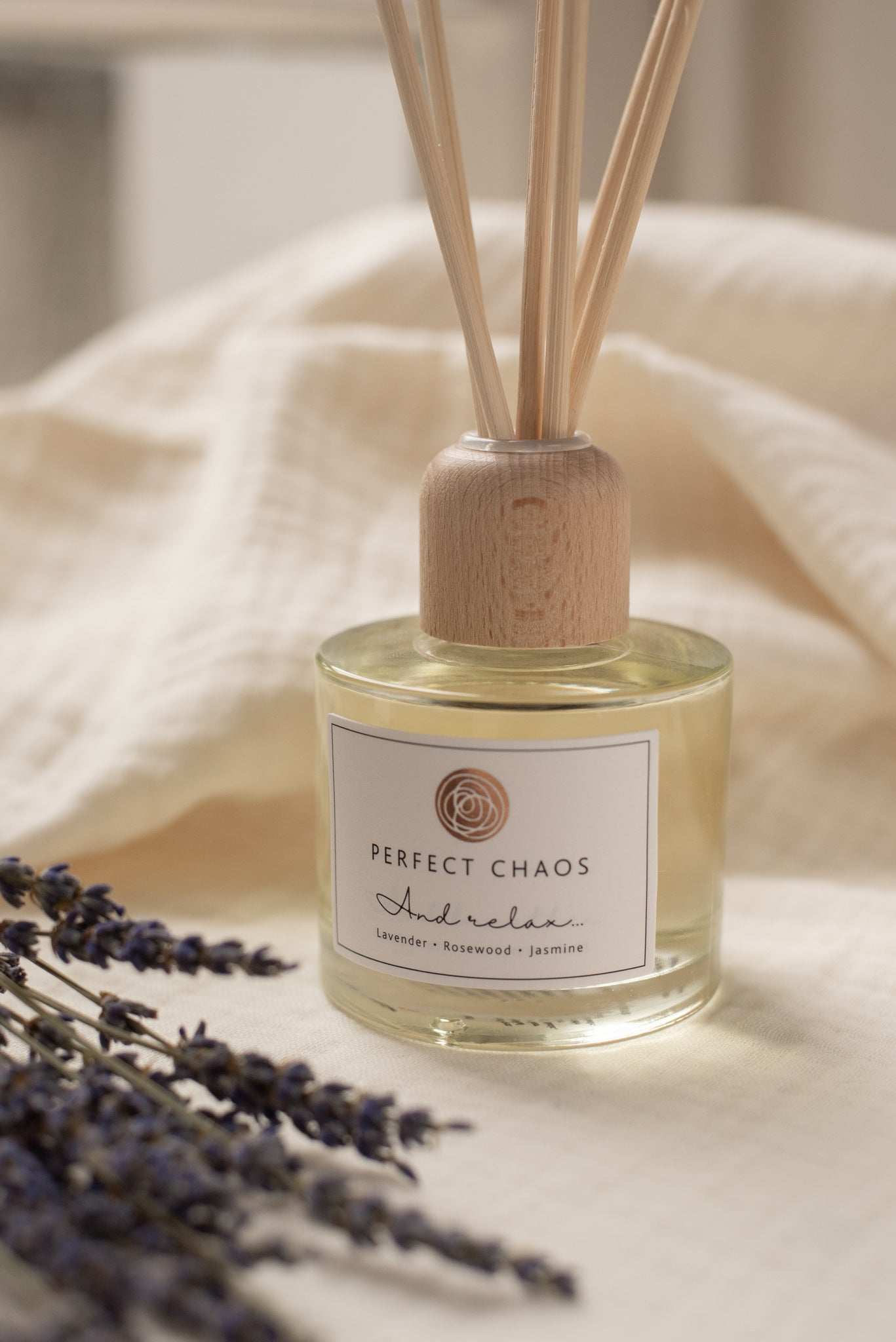 Clear glass reed diffuser and relax with natural wood cap and slender wooden reeds labeled perfect chaos