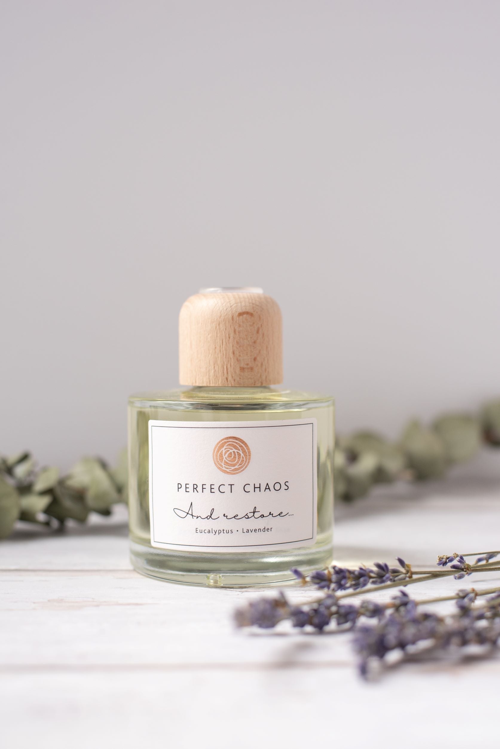 A clear glass reed diffuser with light wood cap and white label featuring perfect chaos and restore eucalyptus lavender essential oils