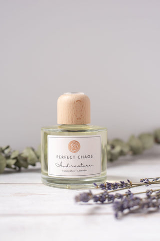 A clear glass reed diffuser with light wood cap and white label featuring perfect chaos and restore eucalyptus lavender essential oils