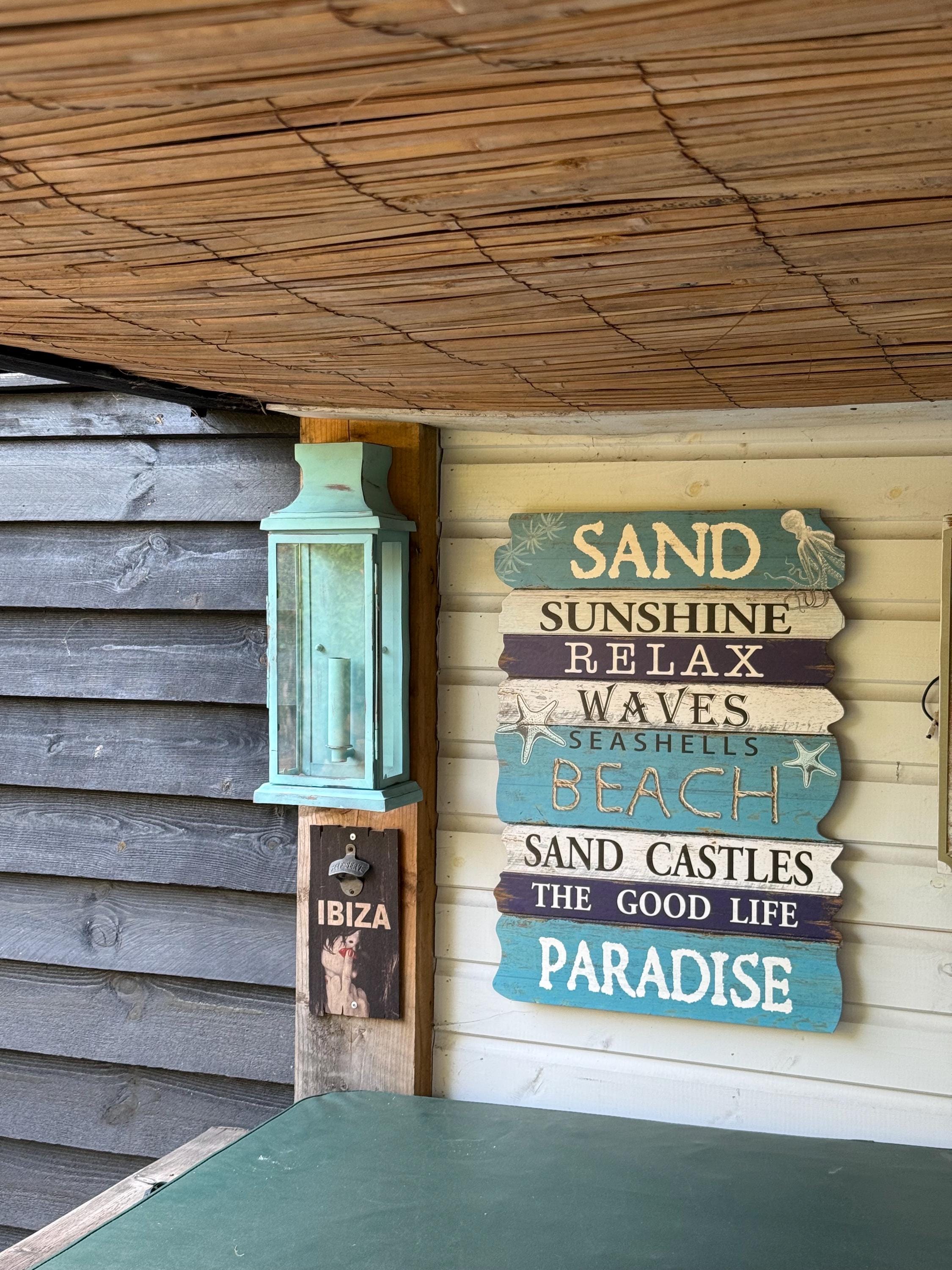 A rustic multi tiered wooden beach sign with teal and purple panels displayed near the reedham verdigris wall light flush mount