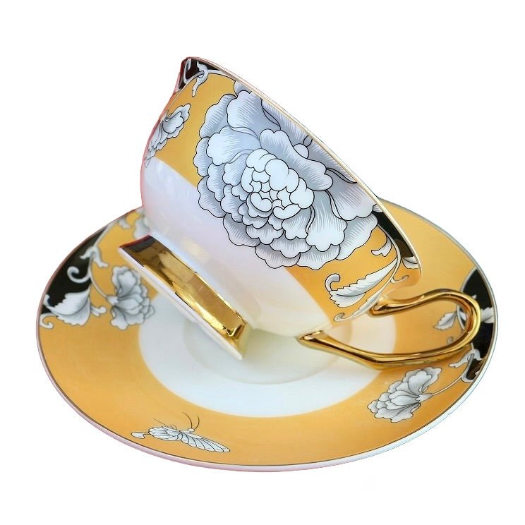 Elegant regal bloom bone china teacup and saucer set with gold rims and large white floral design on yellow background