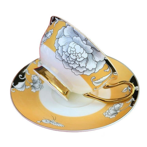Elegant regal bloom bone china teacup and saucer set with gold rims and large white floral design on yellow background
