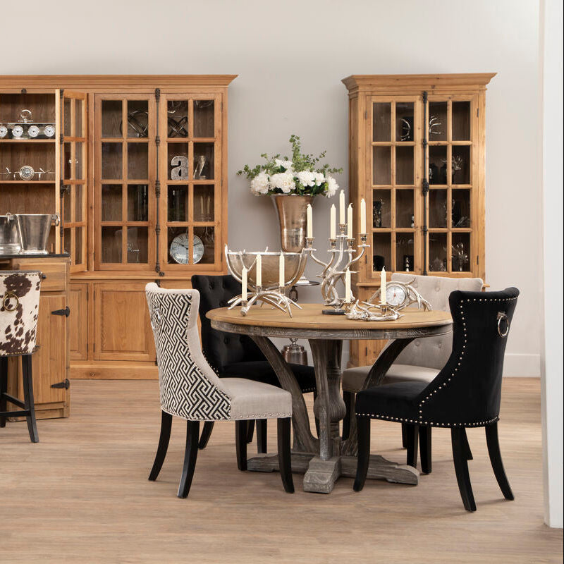 Round wooden dining table with rustic weathered finish and ornate metal legs paired with black cotton velvet chair