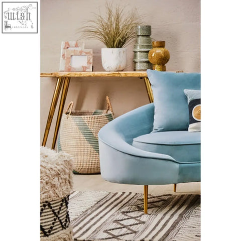 Light blue velvet armchair with gold-tone legs next to a relic petrified wood console table in a modern setting