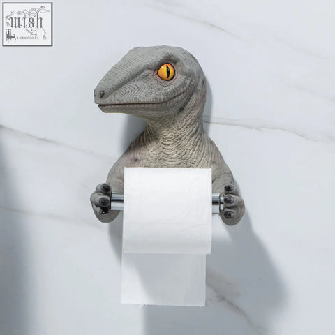 Gray resin dinosaur tissue holder with yellow eyes and textured skin holding white toilet paper roll paper holder