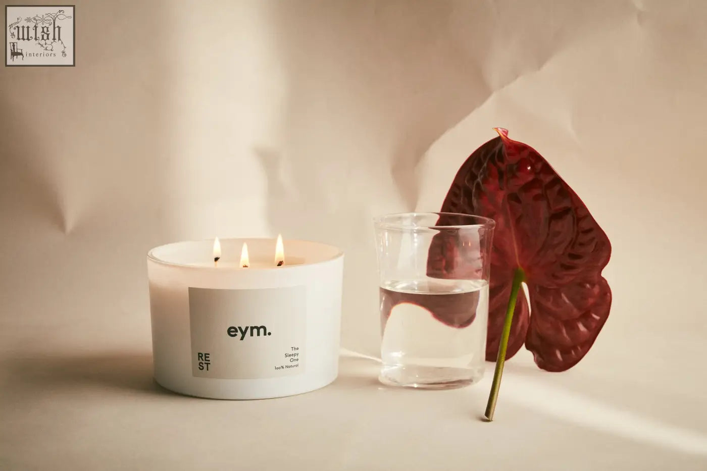 White cylindrical rest three wick candle with minimalist eym label and three lit wicks for relaxation