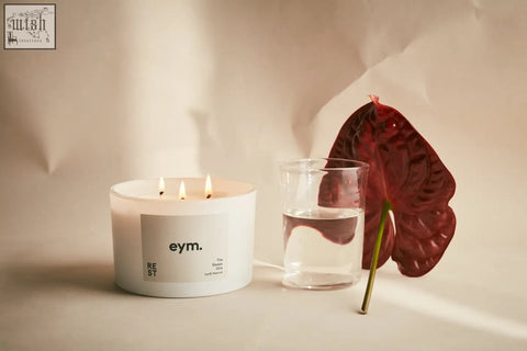 White cylindrical rest three wick candle with minimalist eym label and three lit wicks for relaxation
