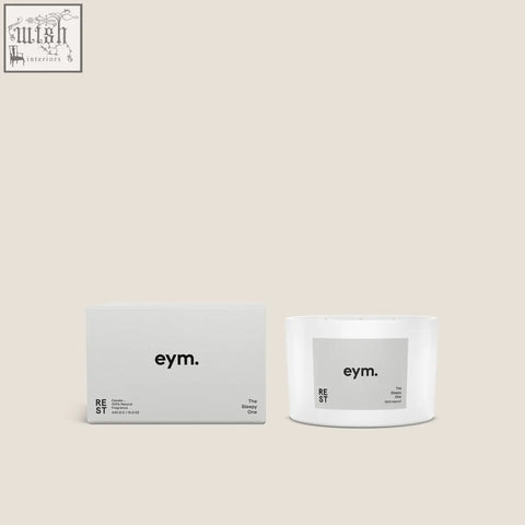 White cylindrical rest three wick candle with a minimalist gray eym label shown with its matching box