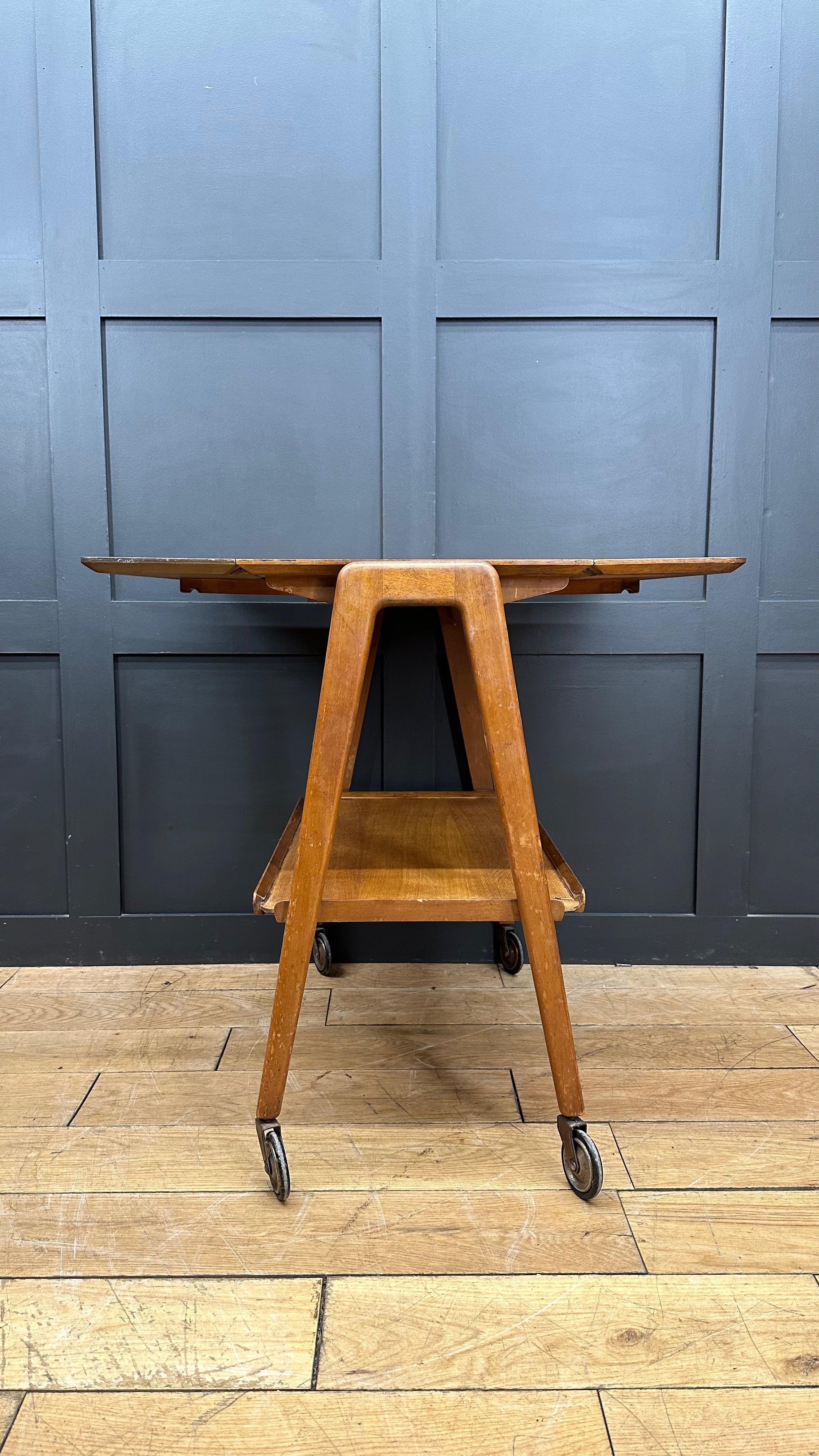 A mid century wooden serving trolley with warm natural finish and four caster wheels perfect for tea cake or cocktails