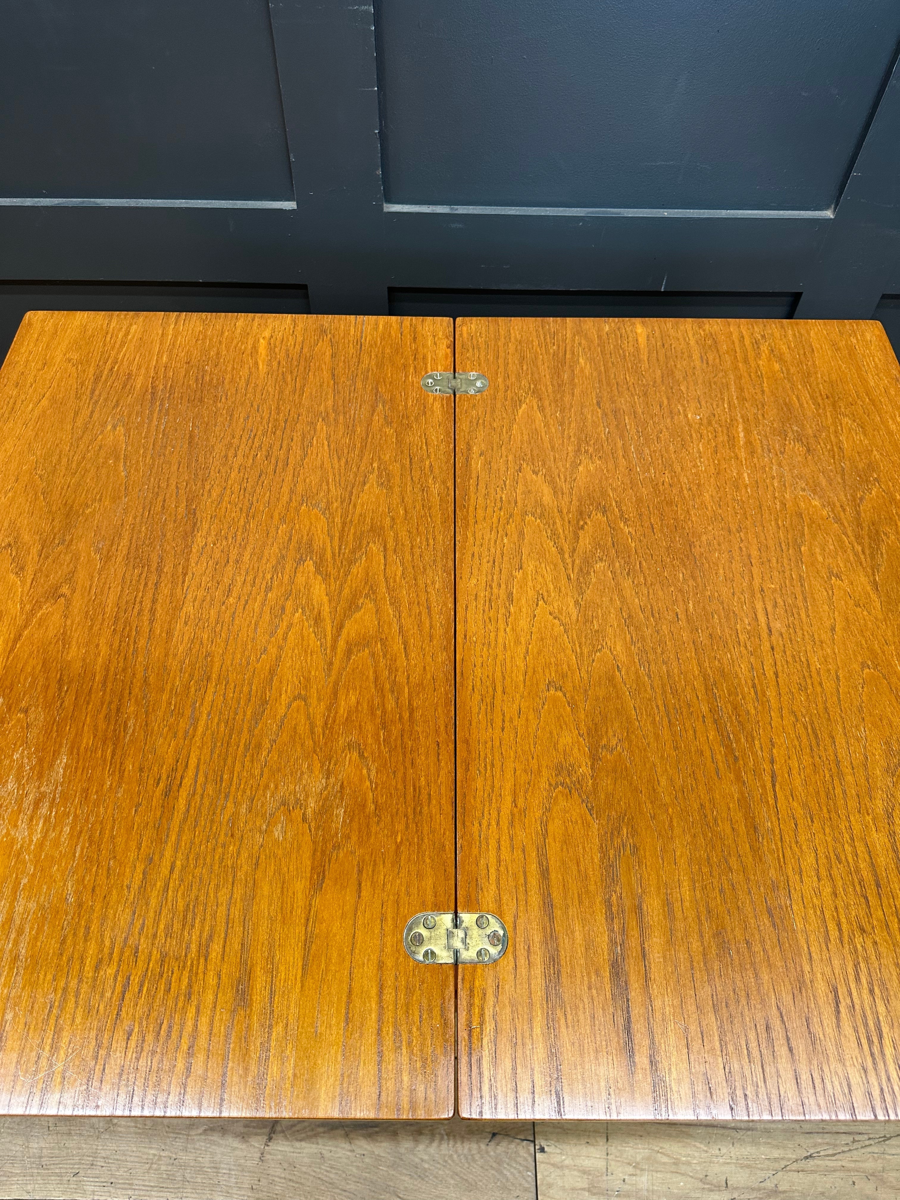 A polished medium brown teak wooden table with brass hinges on a retro mid century serving trolley for tea and cocktails