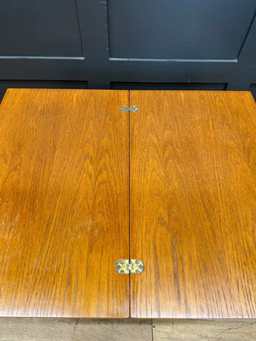 A polished medium brown teak wooden table with brass hinges on a retro mid century serving trolley for tea and cocktails