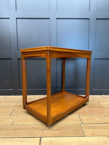 A polished teak wood two-tier mid century side table with a rectangular frame perfect for serving or display