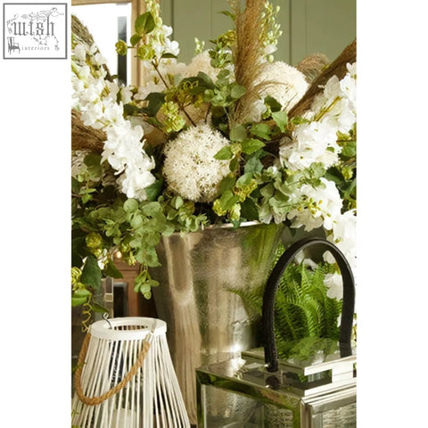 A tall metallic silver finish vase with textured surface holding white flowers in the Reza set of 3 antique silver planters