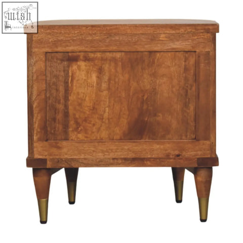 A rustic ribbed bedside table in solid mango wood with an amber oak finish and brass-tipped legs and two ribbed-front drawers